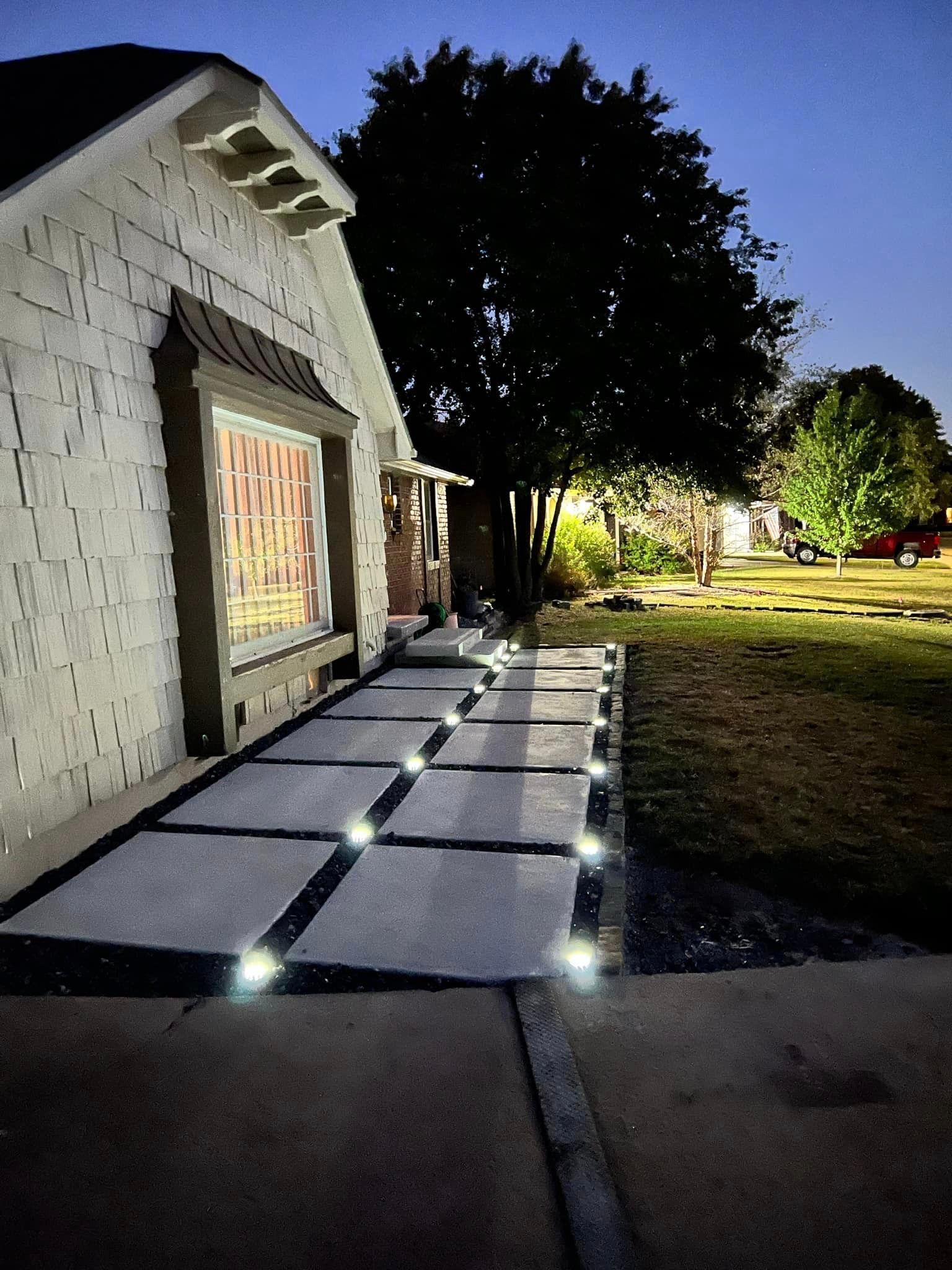 A house with a walkway with lights on it in front of it at night.