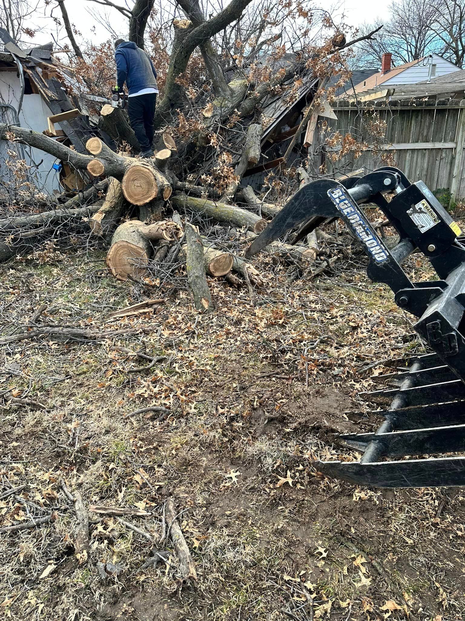A man is standing on top of a pile of logs in a yard.