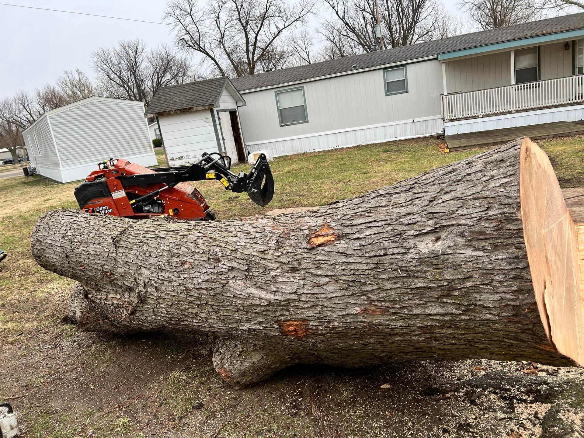 A large log is laying on the ground in front of a house.