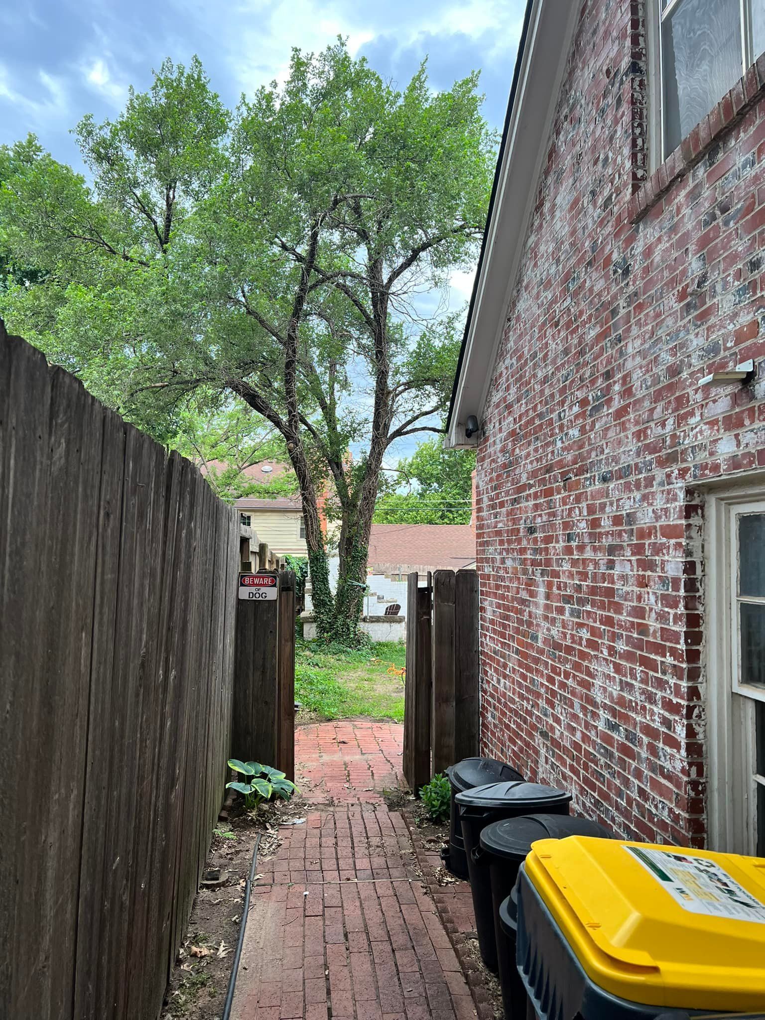A brick building with a wooden fence and a yellow trash can in front of it.