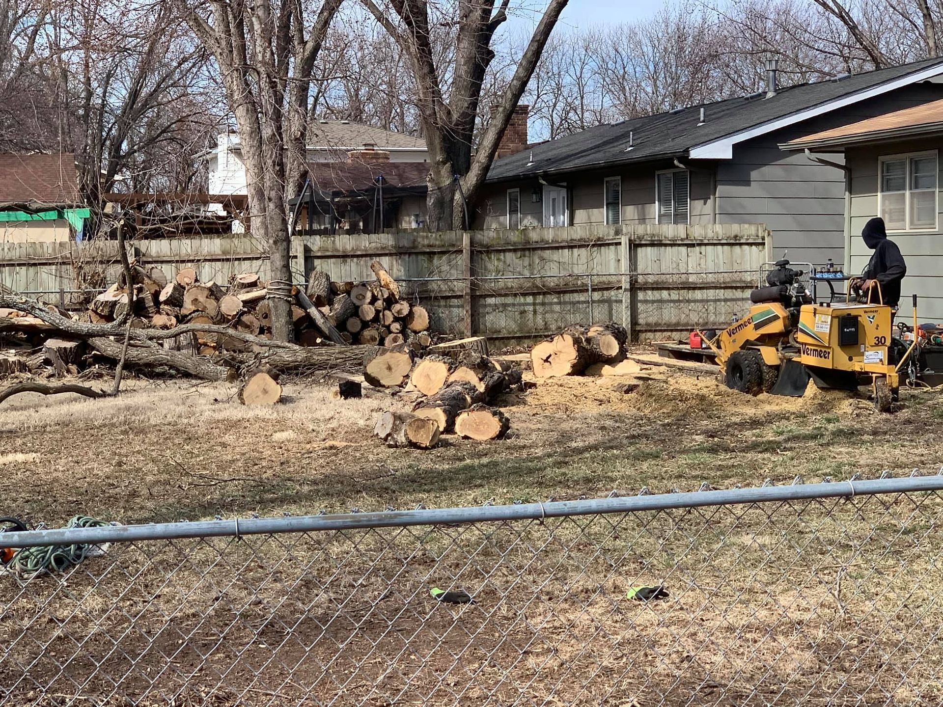 A man is using a stump grinder to remove a tree stump in front of a house.