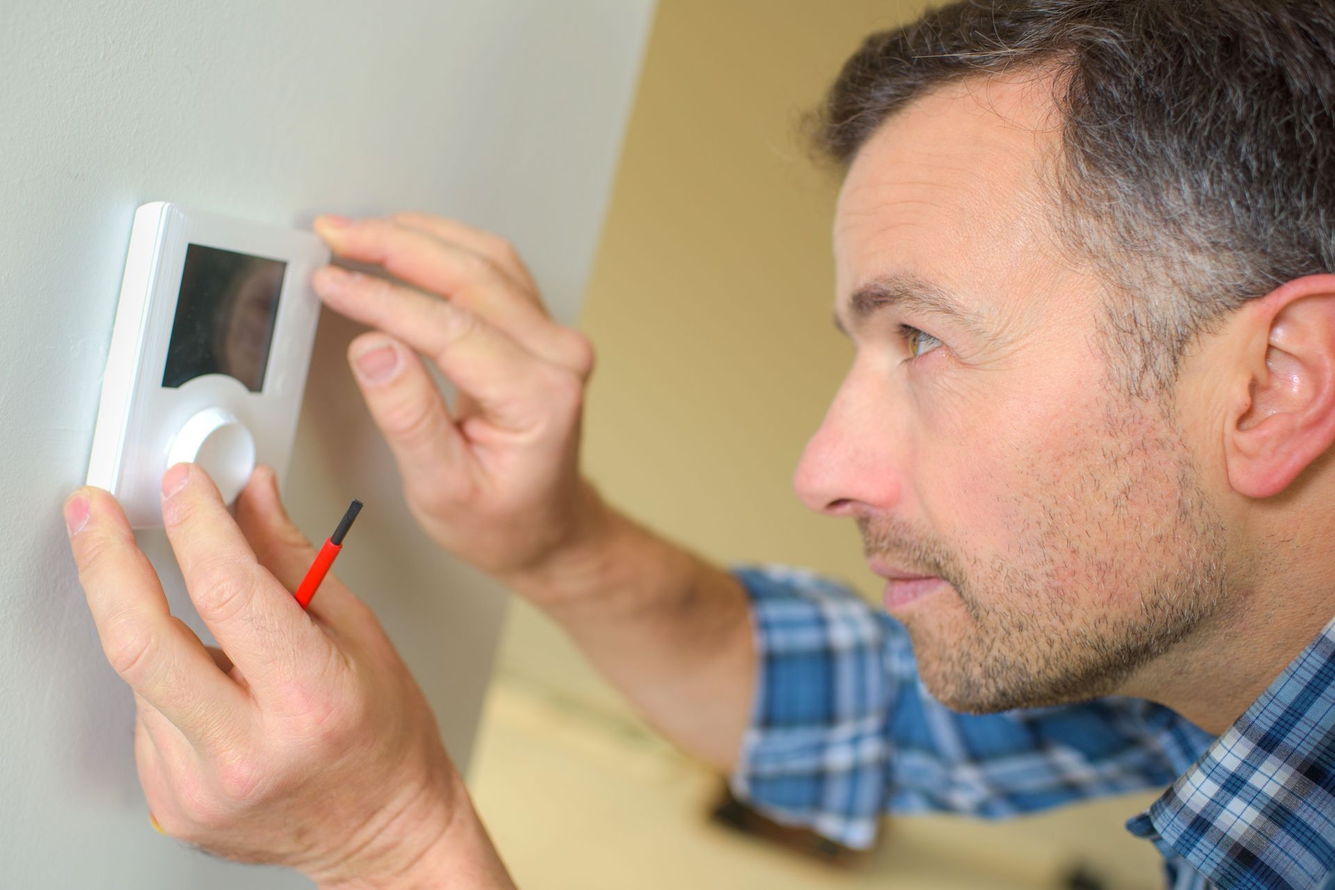 Man installing a thermostat on a wall, using a screwdriver.