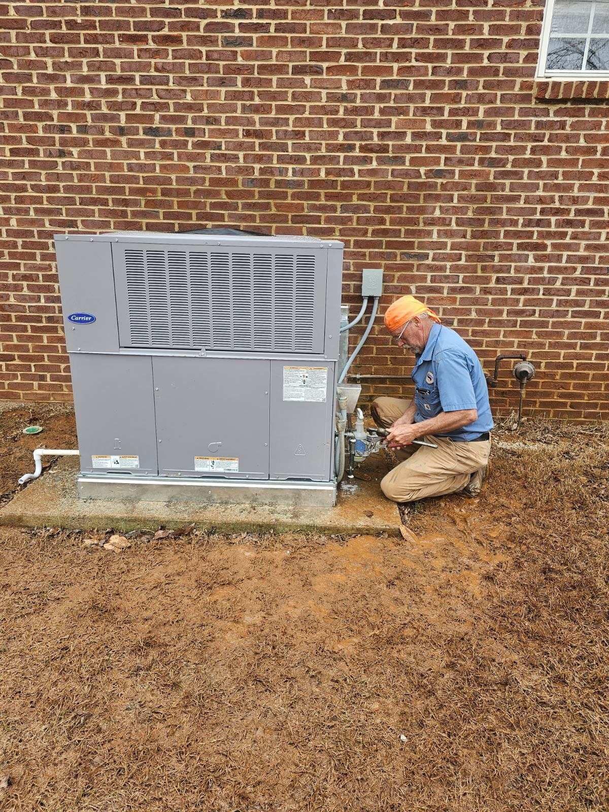 HVAC technician working on an air conditioning unit near a brick wall outdoors.