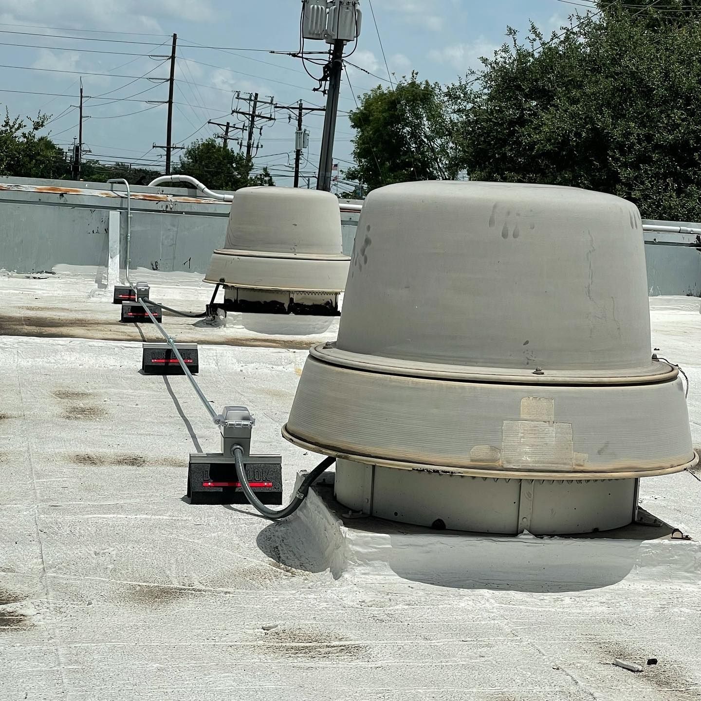Two white roof vents on a weathered flat roof, connected by a cable to small black boxes.