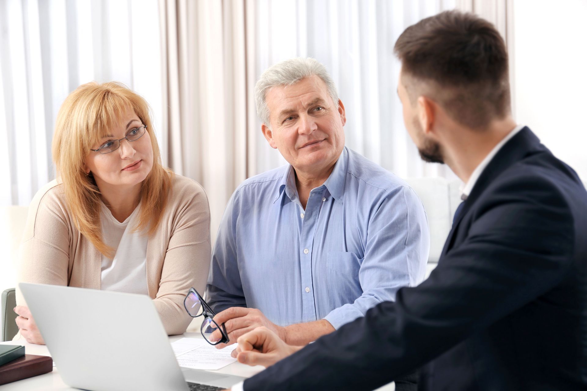 A couple consults with a person in a suit at a table with a laptop, documents, and glasses.