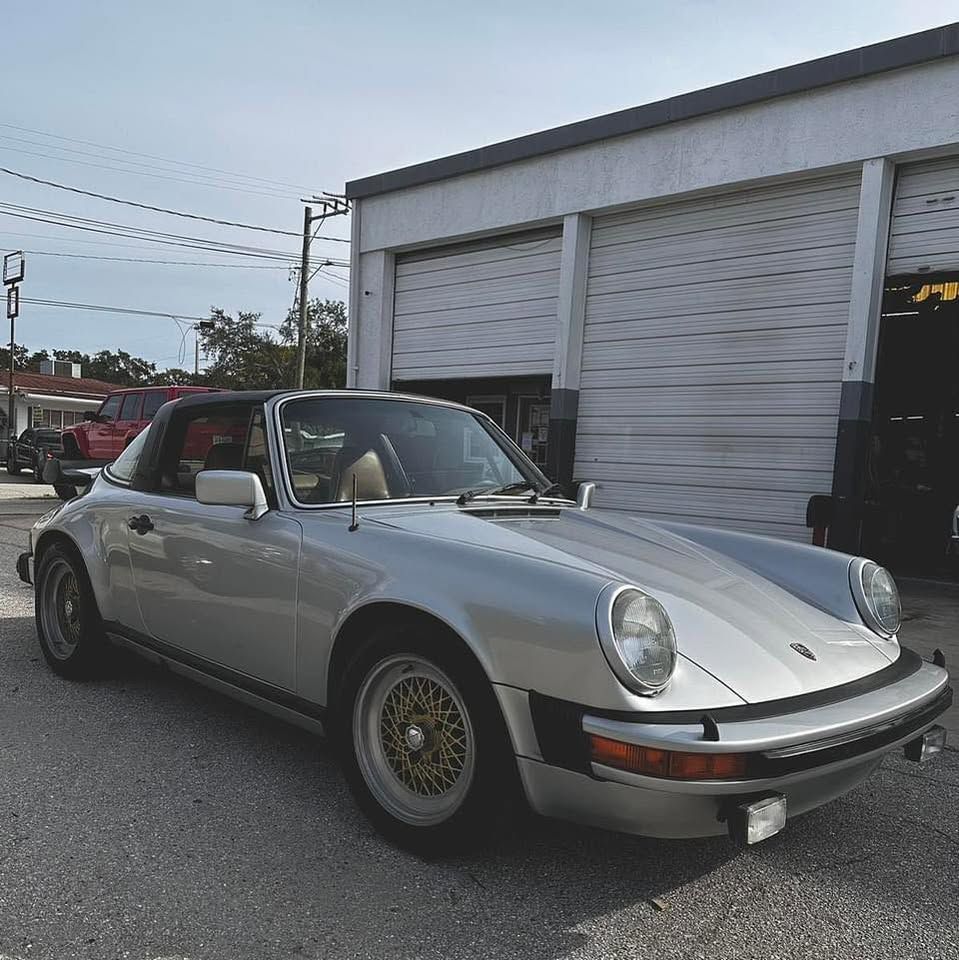 A silver porsche is parked in front of a garage.