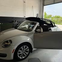 A white beetle convertible is parked in a garage with its doors open.