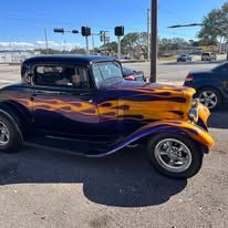 A purple and yellow car with flames painted on it is parked on the side of the road.