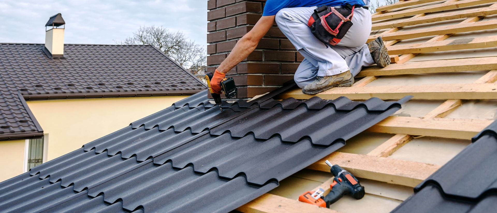 Workers installing dark gray roof tiles on a house roof
