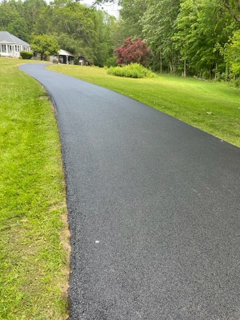A black asphalt driveway going through a lush green field