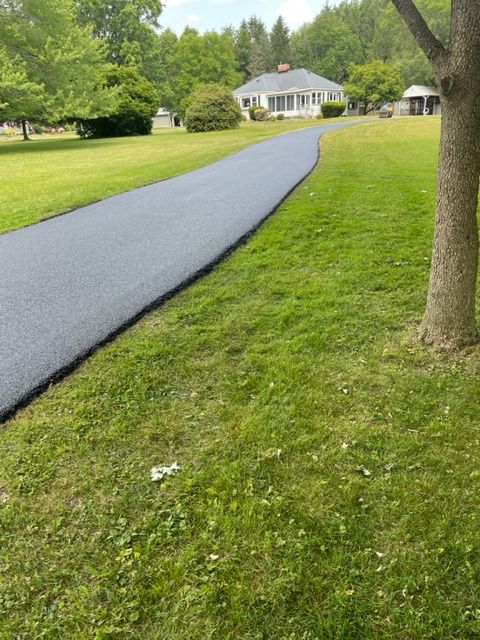 A driveway going through a lush green field with a house in the background