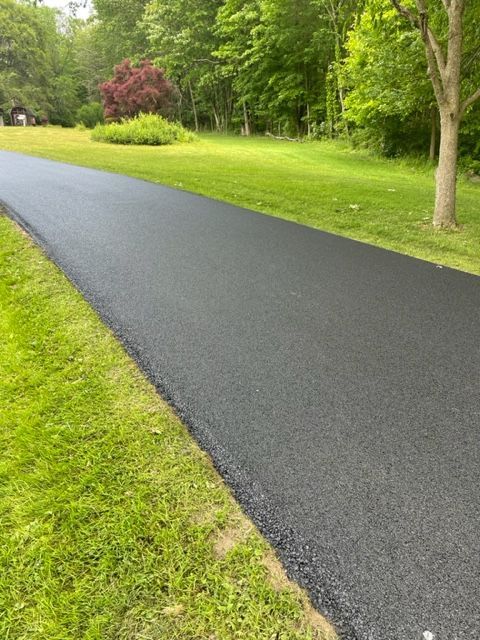 A black asphalt driveway going through a grassy field