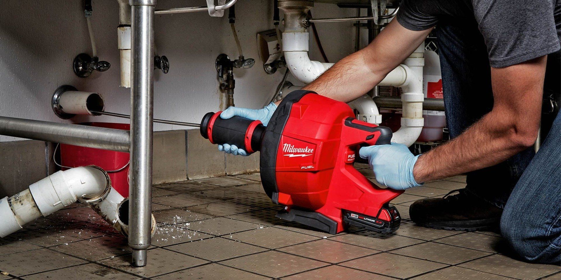 A man is using a drain cleaner to clean a drain under a sink.