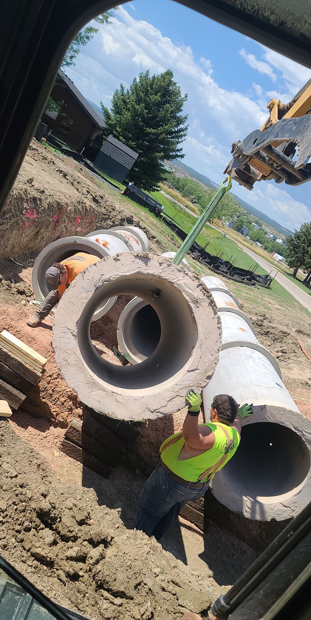 Worker in a neon safety vest hoisting large concrete pipe rings at a construction site