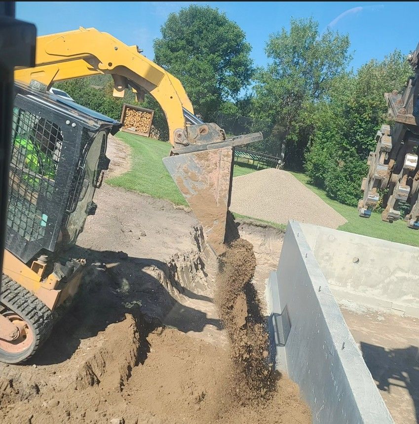 Yellow excavator dumping dirt into a trench beside a concrete foundation on a sunny site