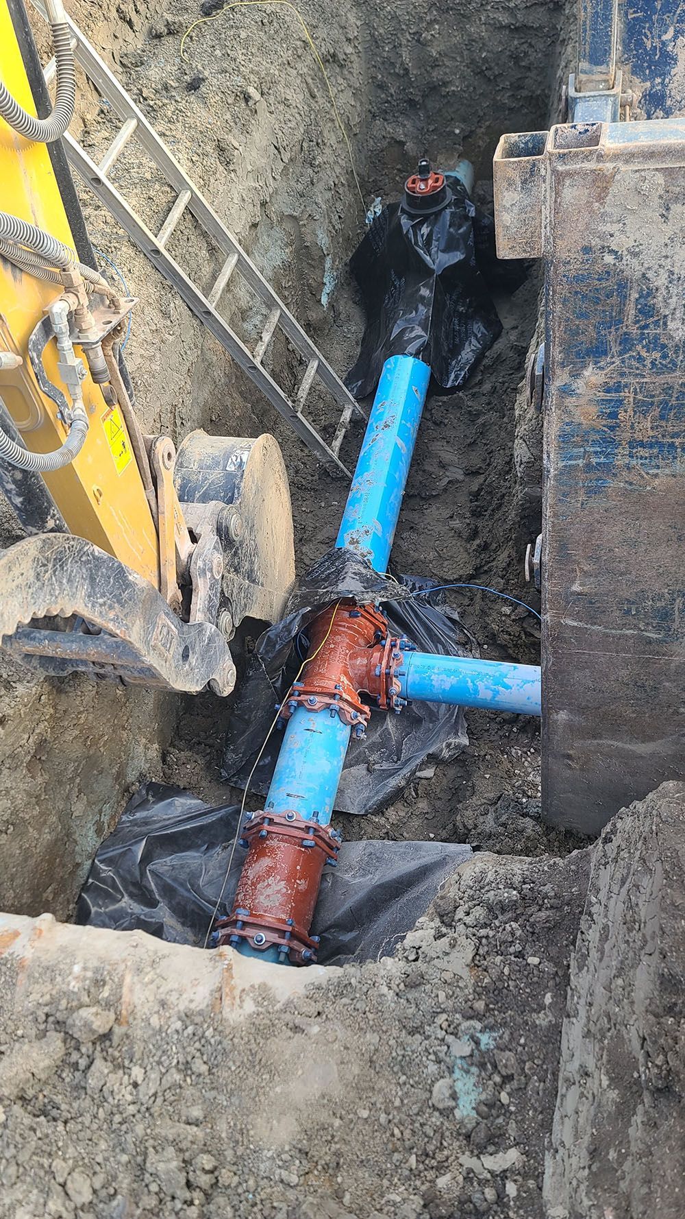 Excavation trench with blue pipes and orange fittings being installed underground