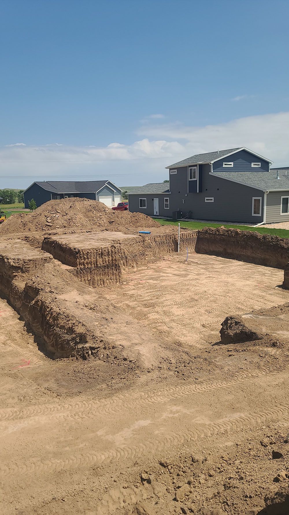 Large dirt excavation site beside new suburban houses under a clear sky