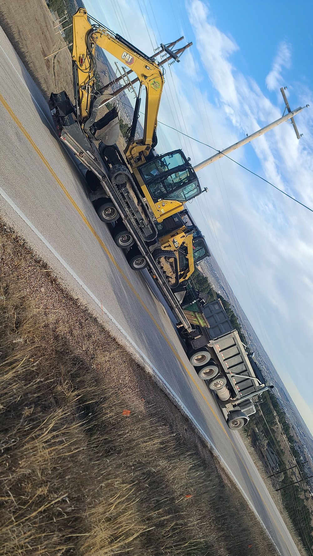 Yellow excavator on a roadside construction site under a blue sky.