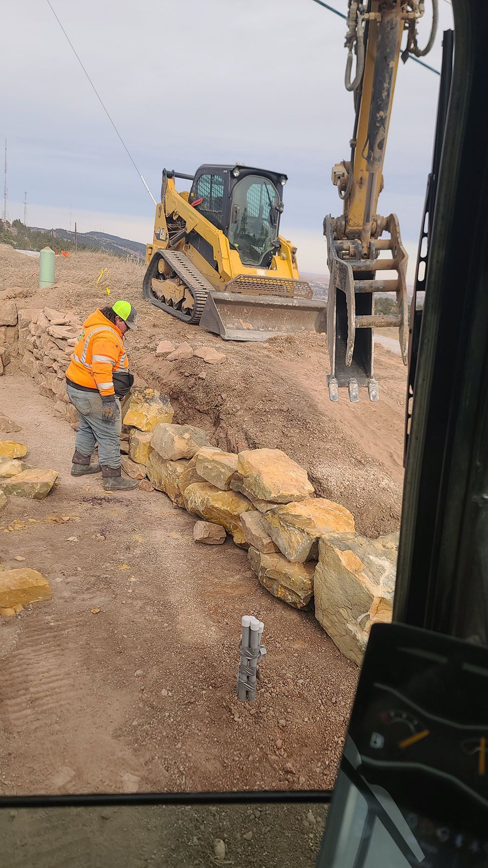 Construction workers and heavy machinery grading a dirt slope at a roadwork site