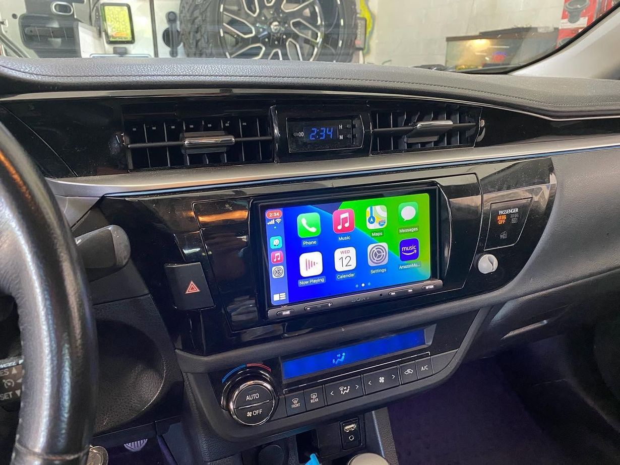 Car dashboard with a lit touchscreen infotainment display and climate controls, viewed from the driver’s seat