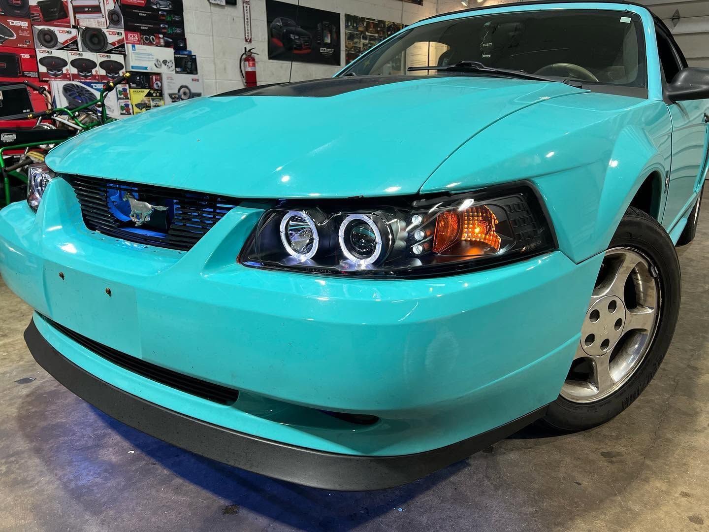 Turquoise Ford Mustang in a garage, front angle with aftermarket headlights