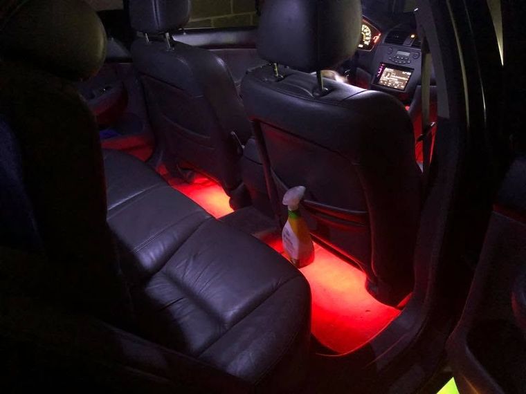Backseat of a car with red floor lighting and black leather seats, with a drink cup in the center.