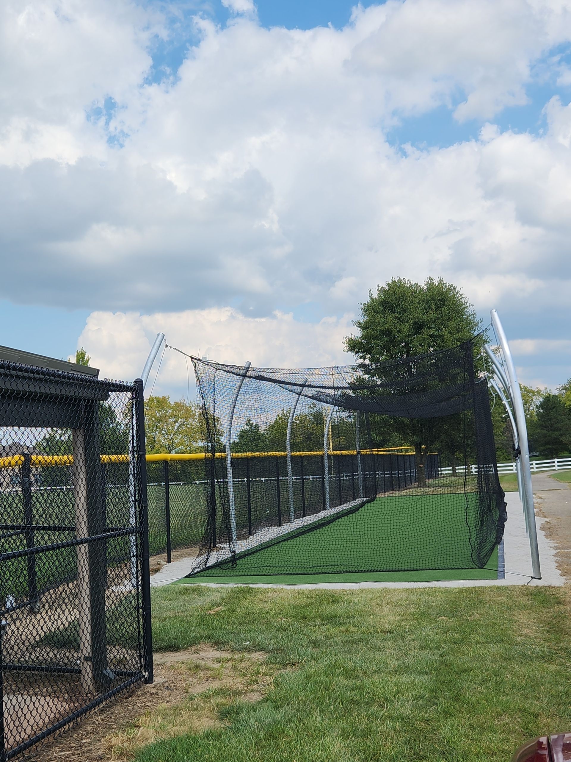 Netted outdoor sports field beside a fence and tree under a cloudy sky