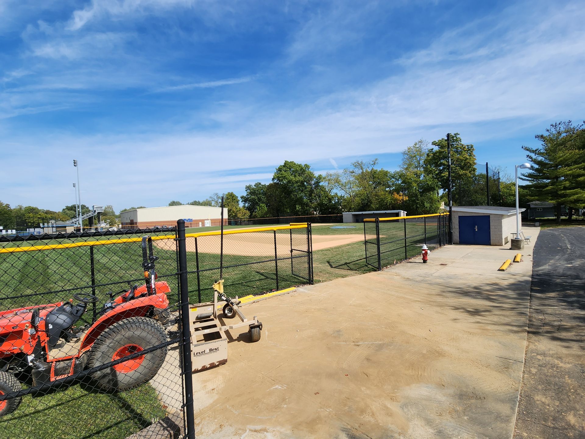 Construction site with orange excavator, fenced dirt lot, and small white shed under a blue sky