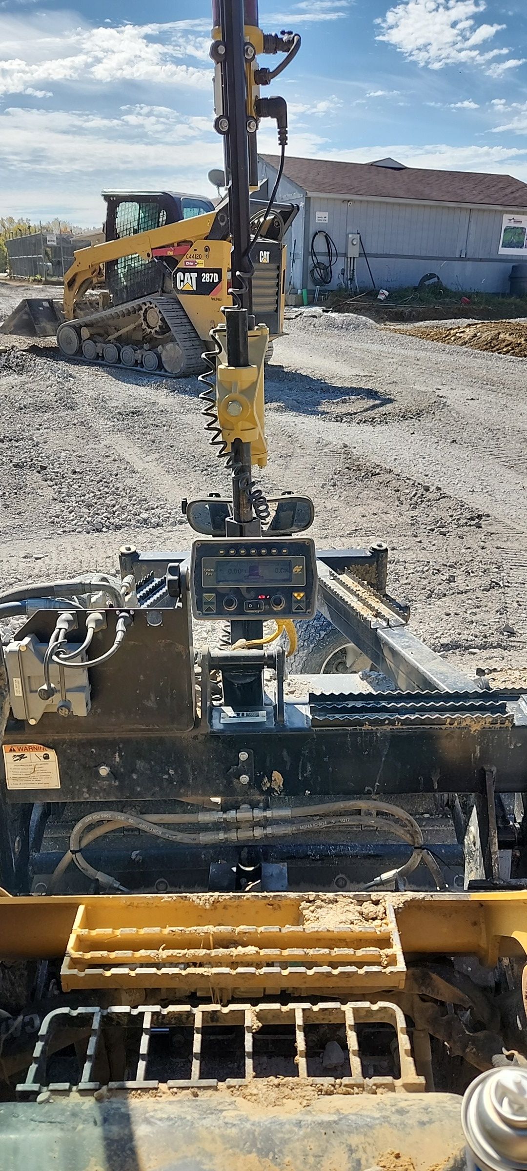 Excavator bucket and arm working in a gravel lot with another excavator and a building in the background