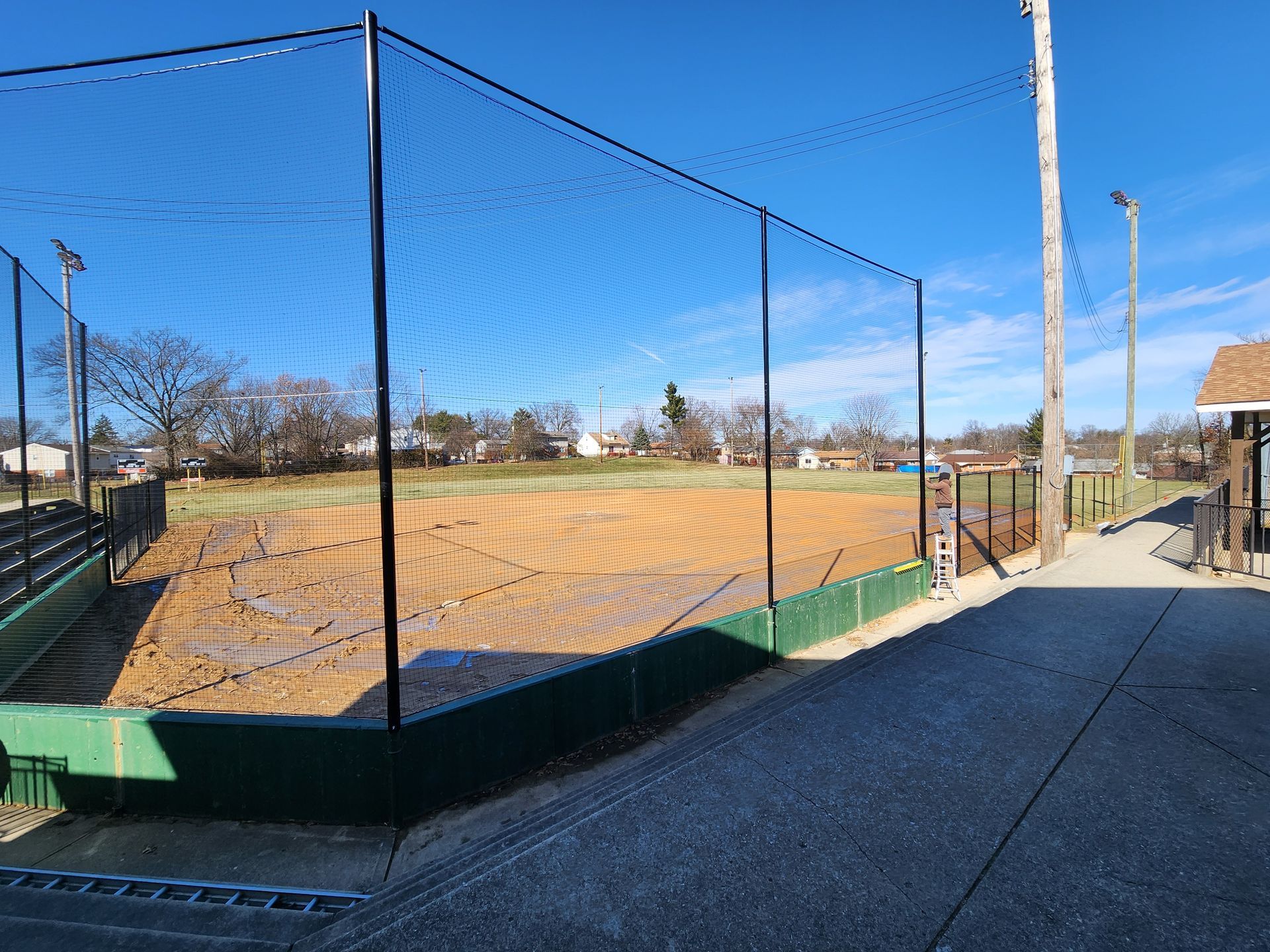 Baseball field with chain-link backstop, dugout fencing, and a clear blue sky