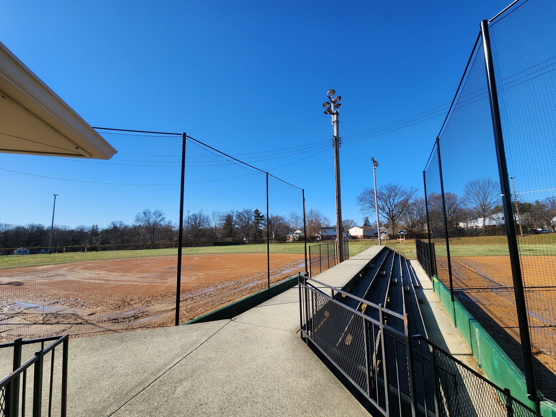 Sunny baseball field with chain-link fences, dugout benches, and a clear blue sky