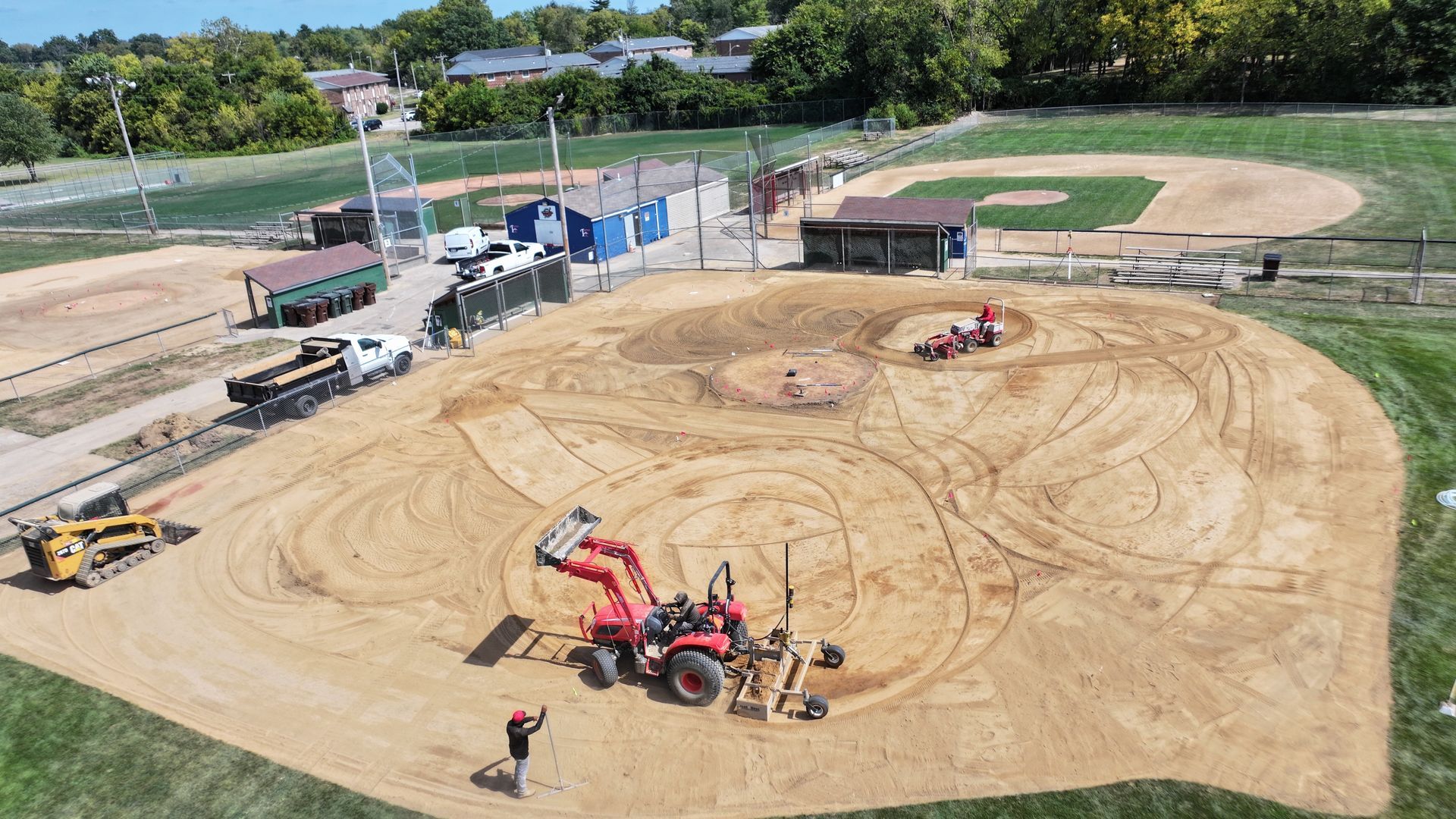 Aerial view of a dirt baseball field under construction with heavy equipment and workers.