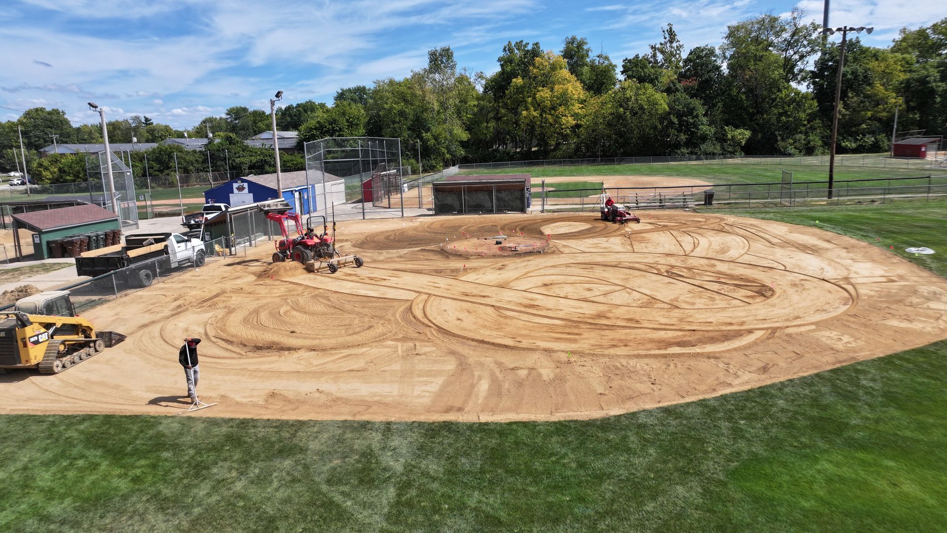 Construction site with bulldozers leveling a large dirt area beside a grassy field and trees