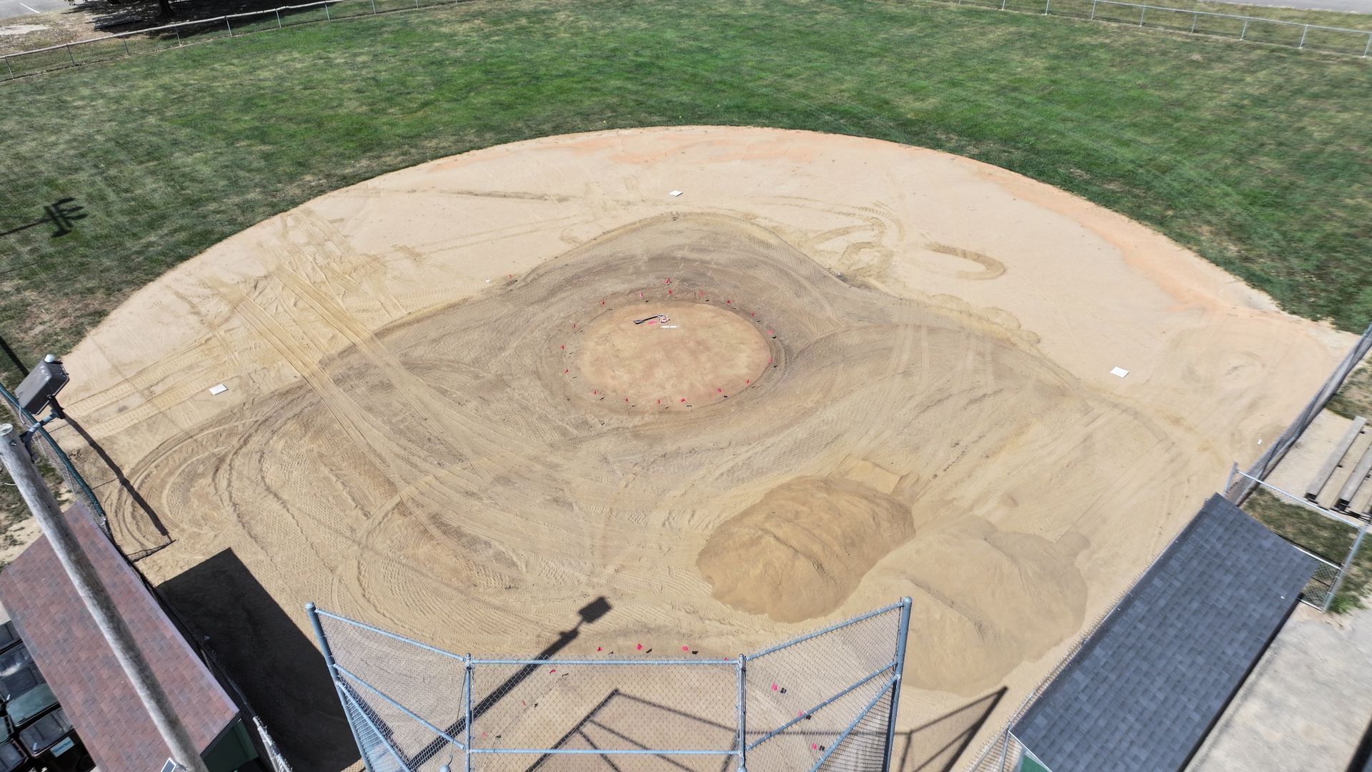 Empty baseball field dirt infield with circular pitcher's mound, viewed from behind the backstop