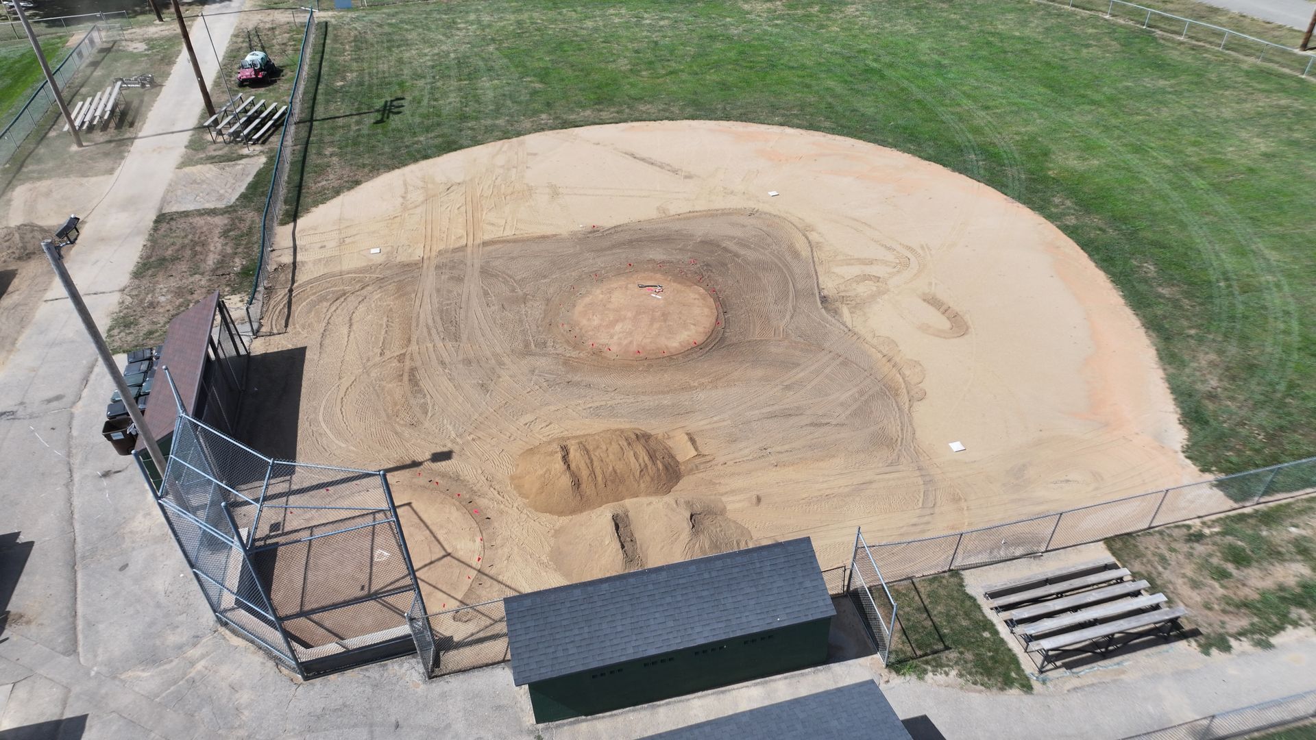 Aerial view of a baseball field with a dirt infield and grassy outfield, next to a fenced walkway.