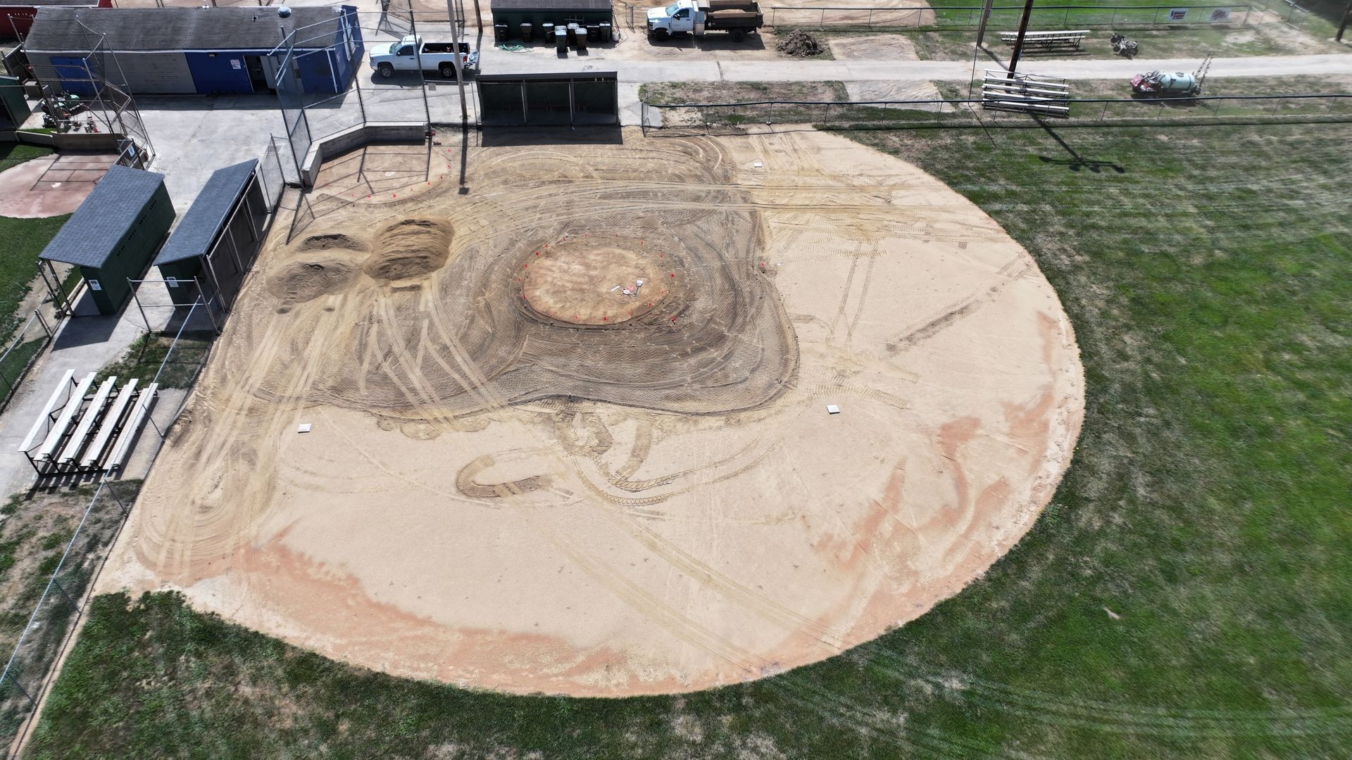 Aerial view of a dirt construction pad in a grassy field with parked vehicles and materials nearby