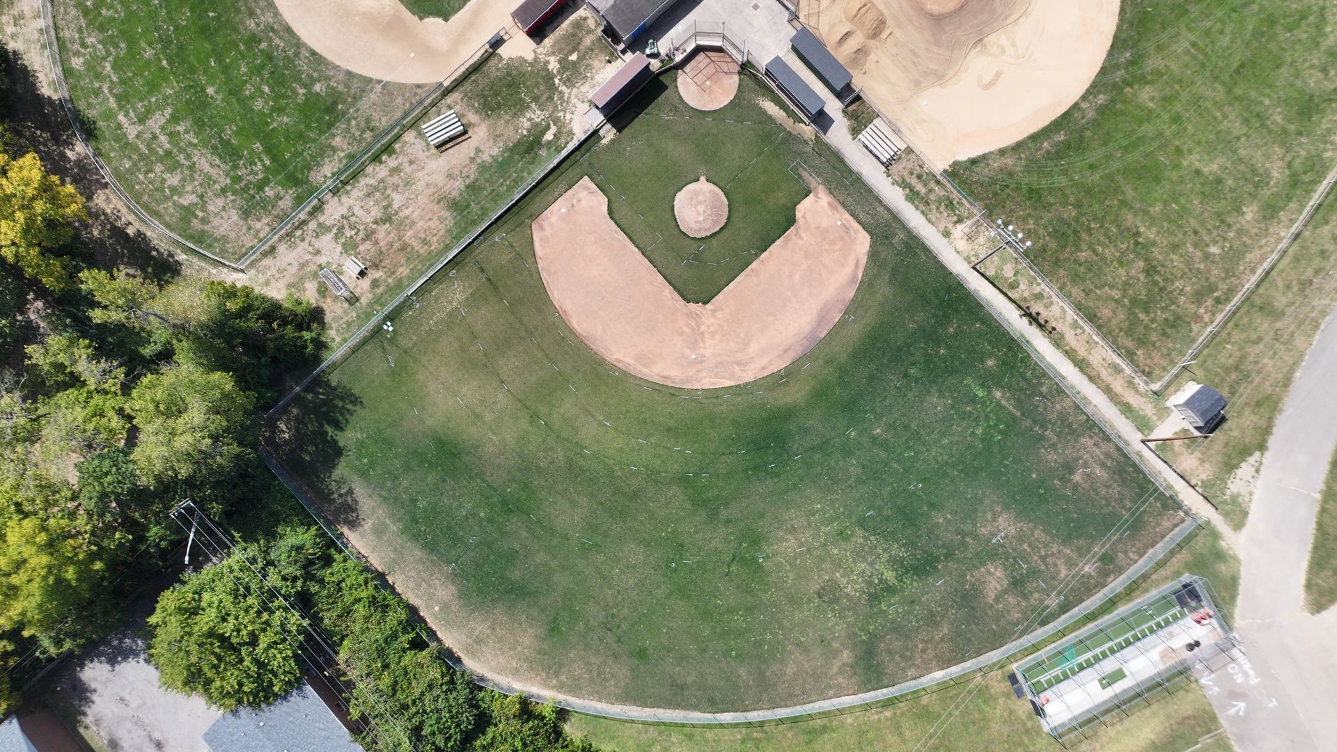 Aerial view of a baseball field with a dirt infield, green outfield, and surrounding trees and paths