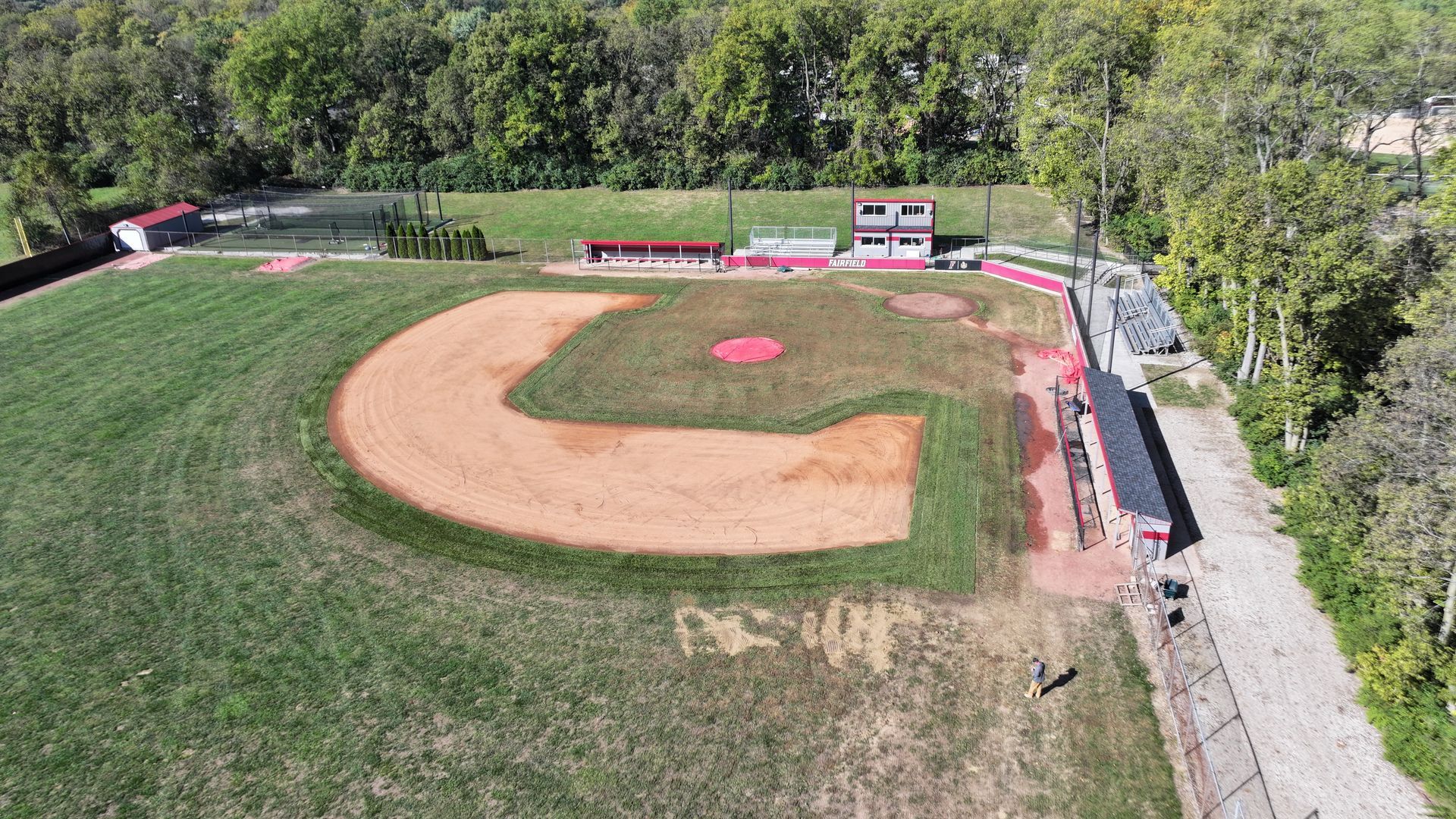 Aerial view of a baseball field with green grass, dirt infield, and surrounding trees.