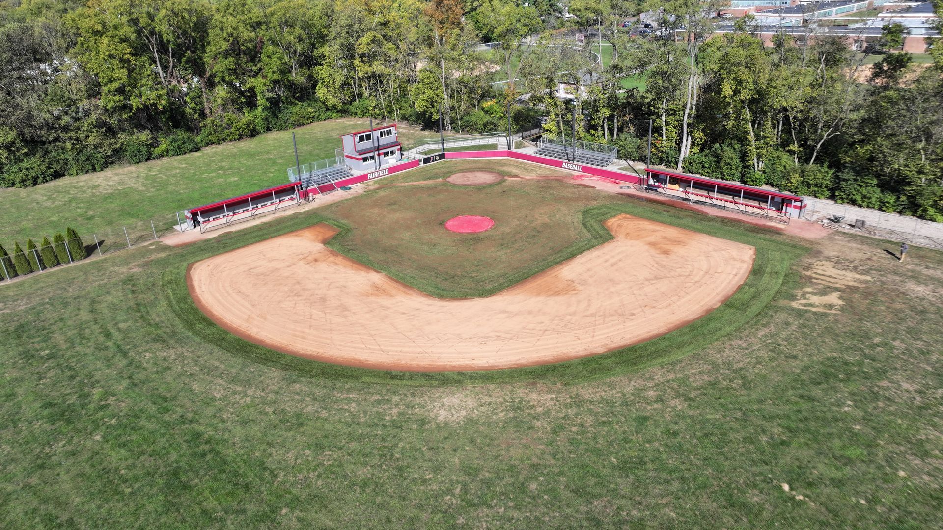 Aerial view of a baseball field with a dirt infield, green outfield, and red dugout fencing.