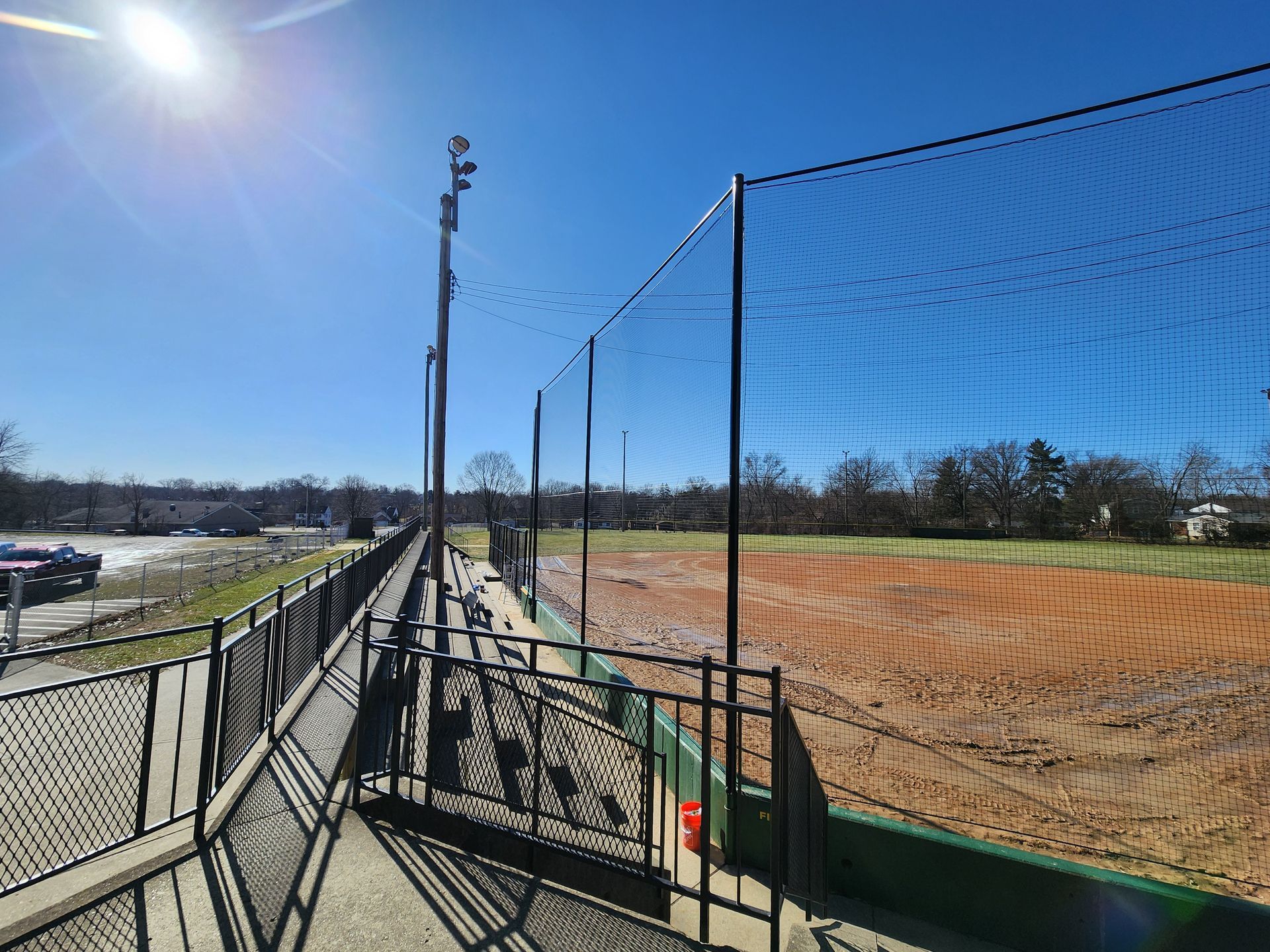 Sunny baseball field behind chain-link fence with bleachers along the left side