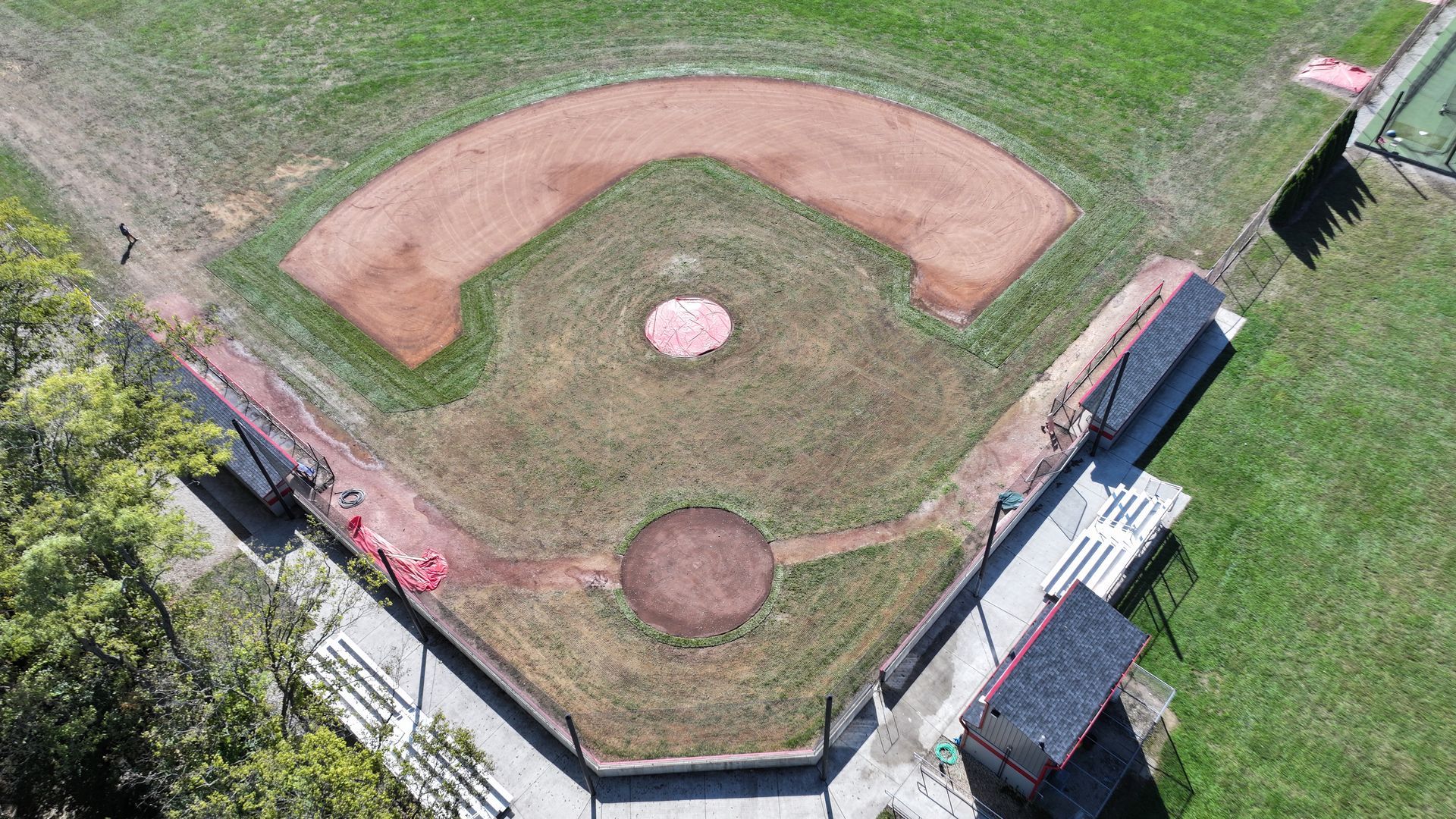 Aerial view of a baseball field with red infield dirt, green grass, and dugouts along the right side