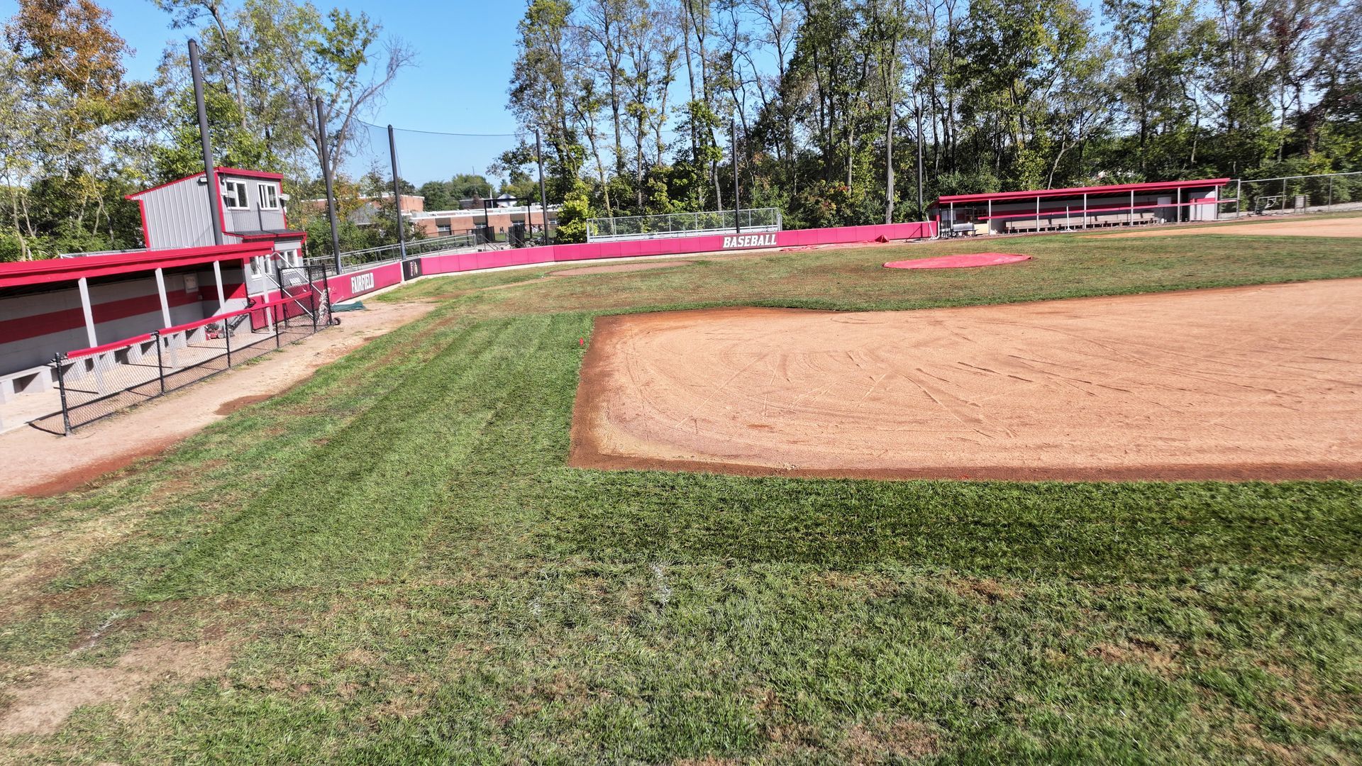 Baseball field with green grass, dirt infield, and red fence under a clear sky