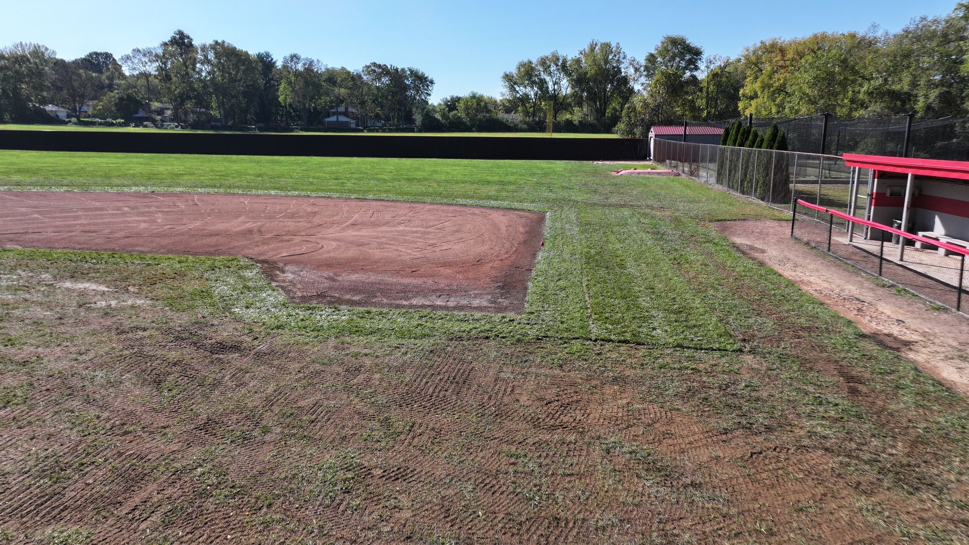Baseball field with dirt infield, green outfield, and red bleachers under a clear sky