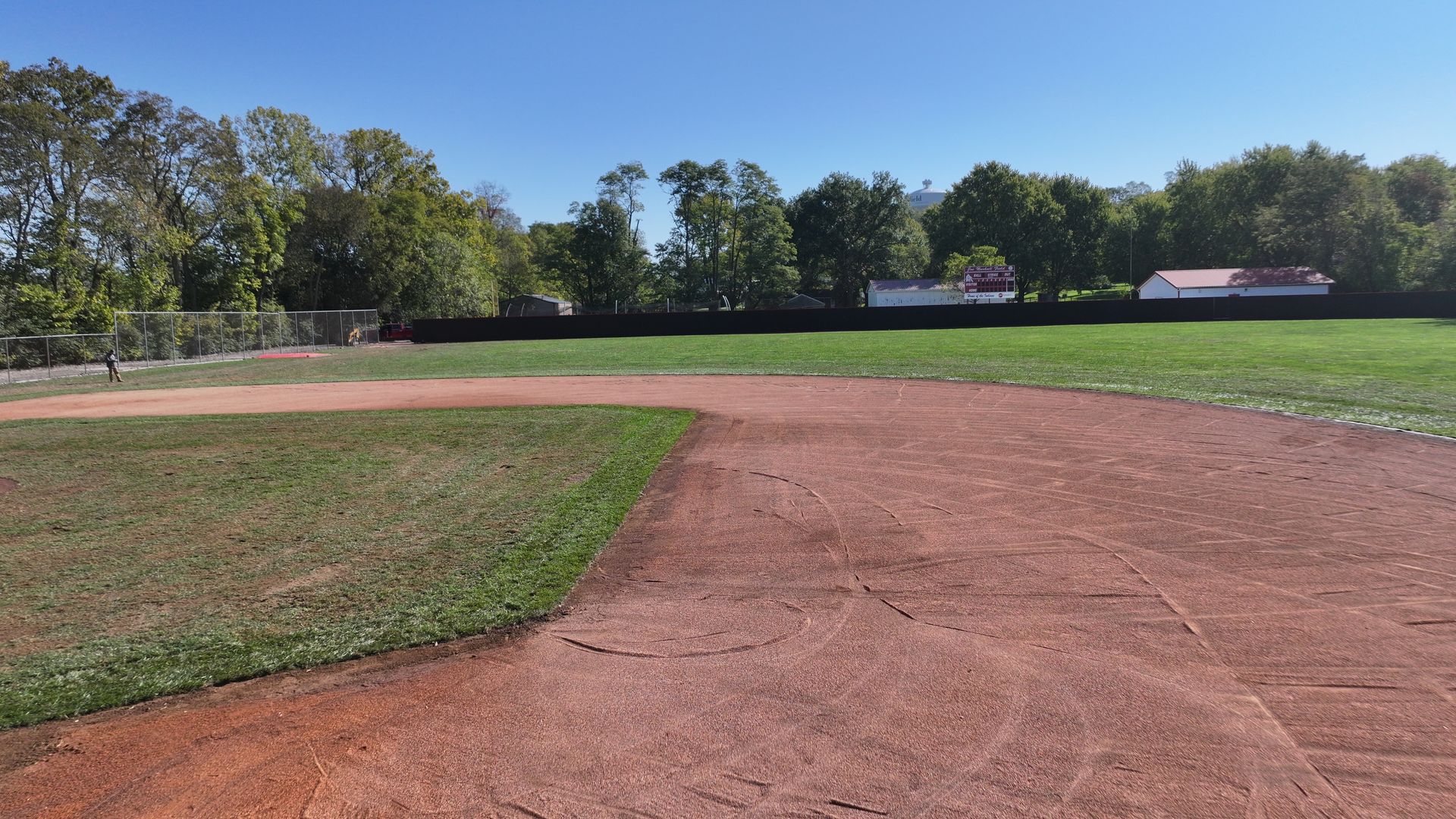 Baseball infield with red dirt and green grass under a clear blue sky