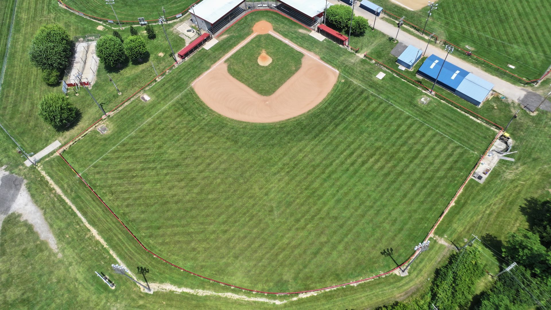 Aerial view of a baseball field with a diamond, green outfield, and surrounding trees and buildings