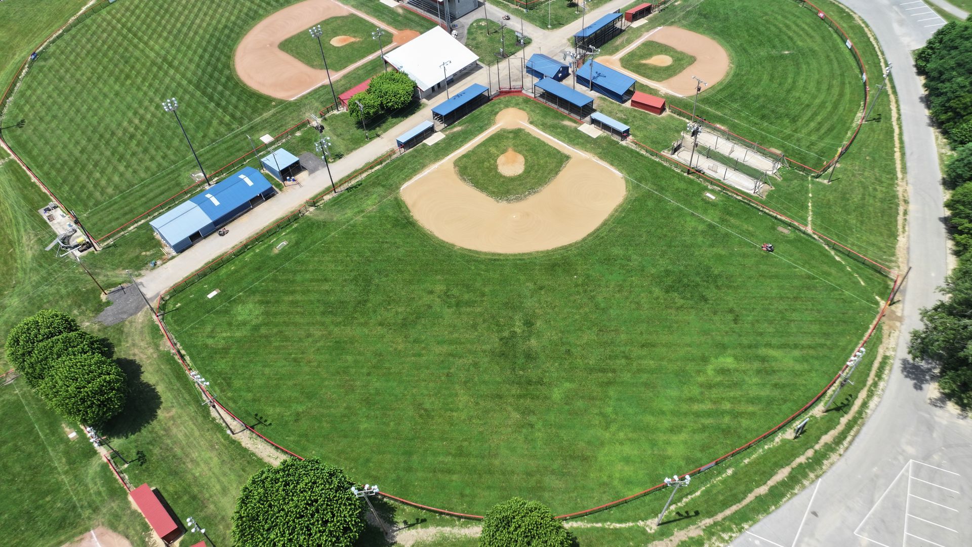 Aerial view of a baseball field complex with green outfield, dirt diamonds, and surrounding trees.