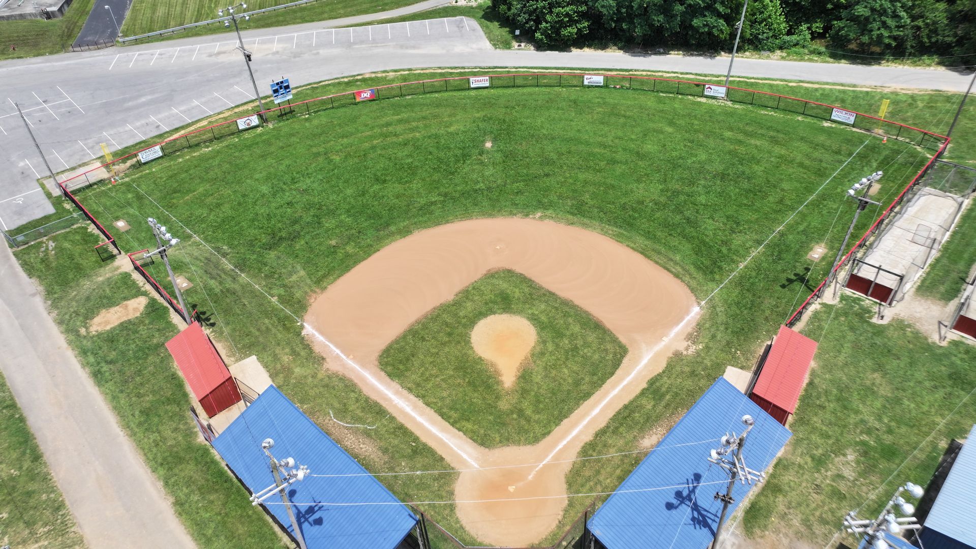 Aerial view of a baseball diamond with blue dugouts and green outfield under bright daylight