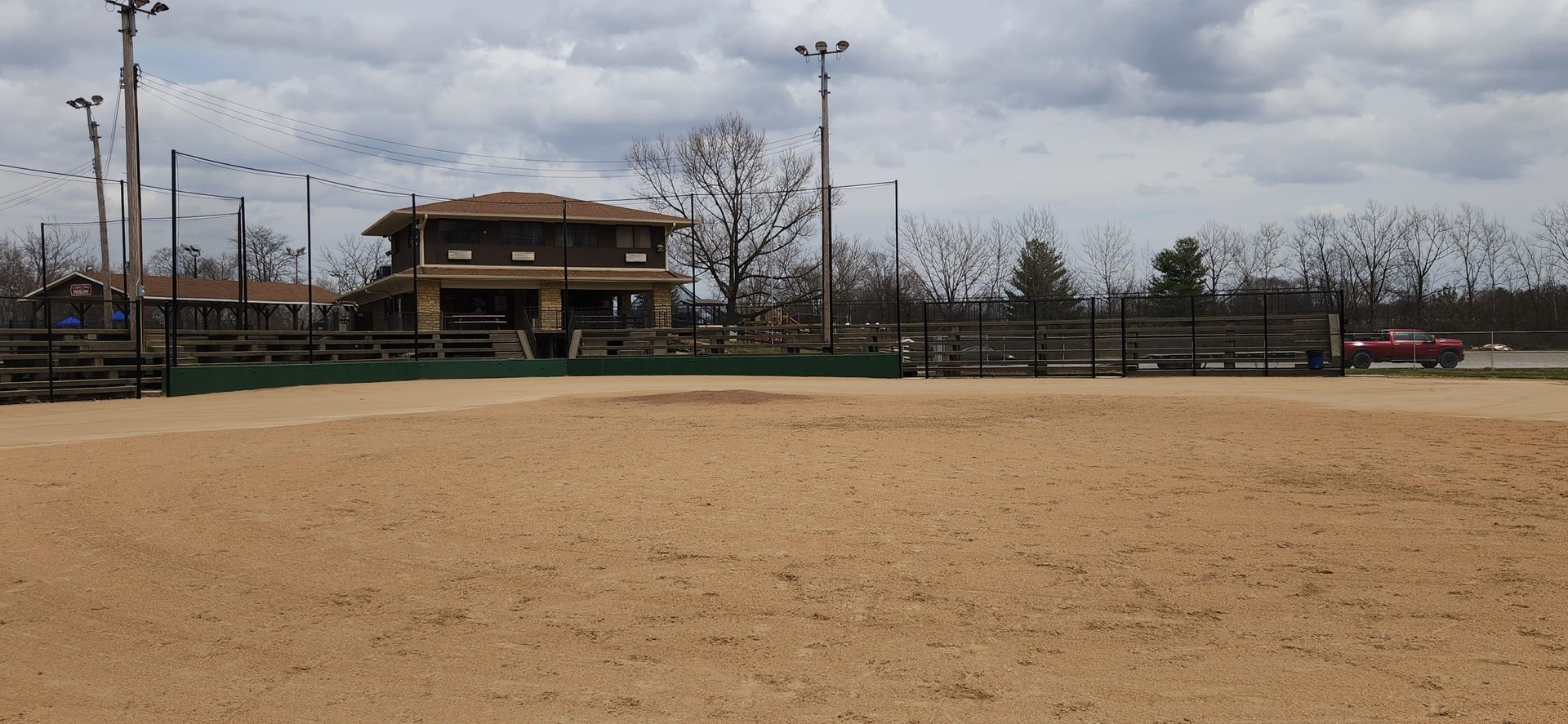Empty sandy sports field with a small building and bare trees under a cloudy sky