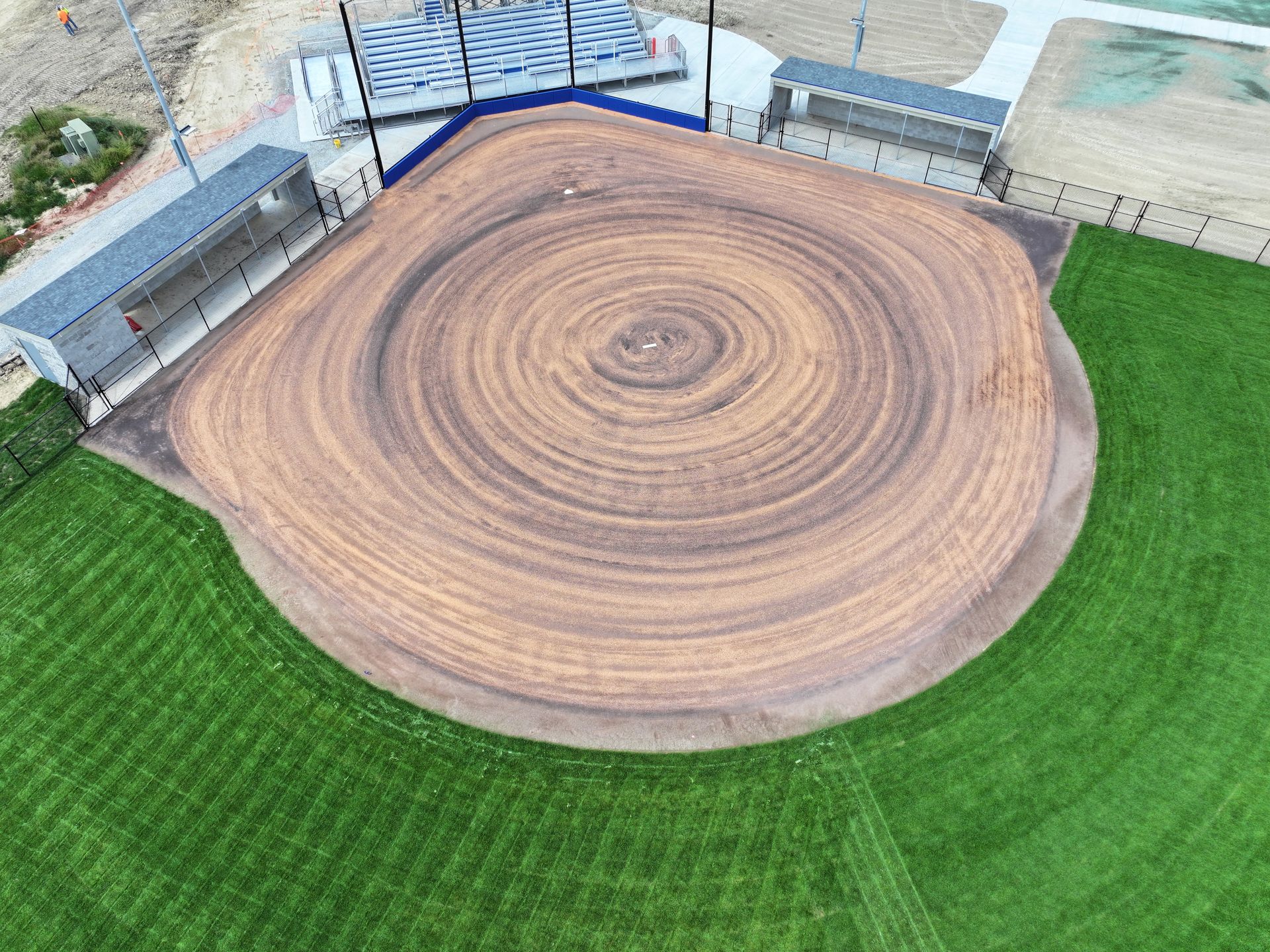 Aerial view of a circular wooden stage with concentric rings, surrounded by green grass and walls.