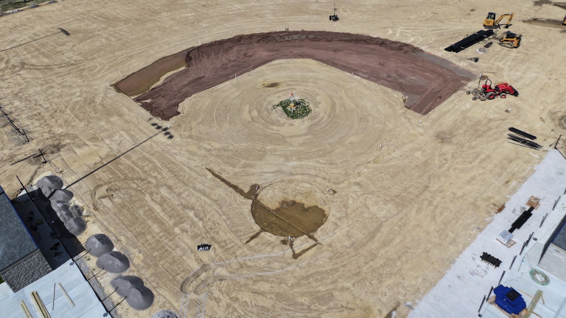 Aerial view of a dirt construction site with an excavated curved trench and heavy equipment nearby